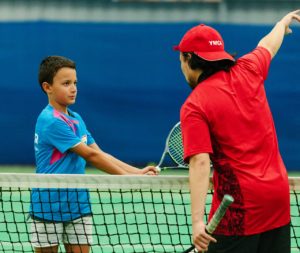 A tennis coach showing a young person how to swing a racquet