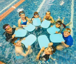 Eight young people with boards in a circle in a pool looking up at the camera