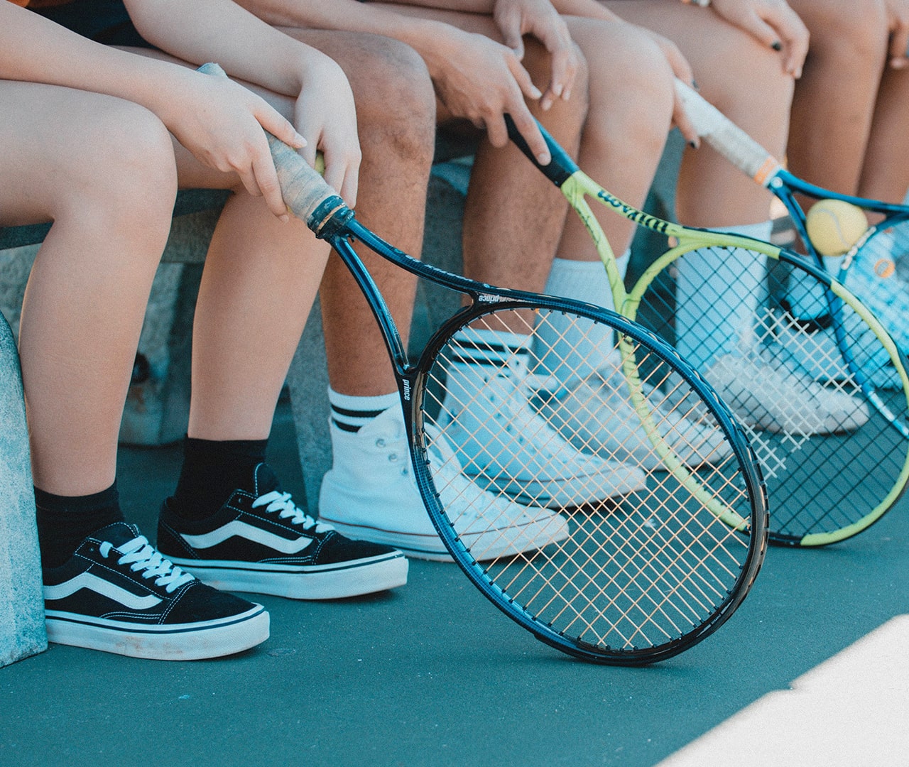 Row of seated tennis players with the top of their racquets resting on the ground