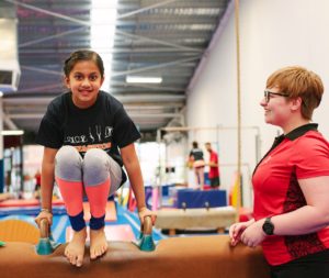 A young person being instructed on the pommel horse