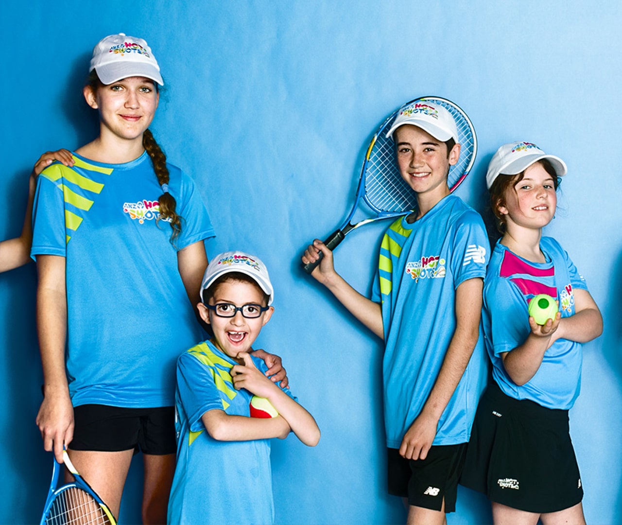 Four children, smiling at the camera, dressed for tennis and holding their racquets or tennis balls
