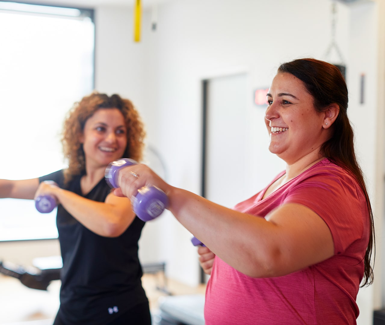 Two ladies smiling and doing an exercise with hand weights