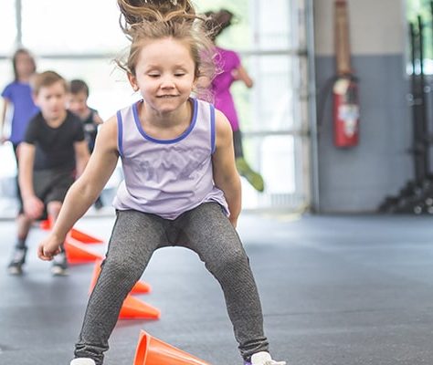 Young children jumping over cones in the gym
