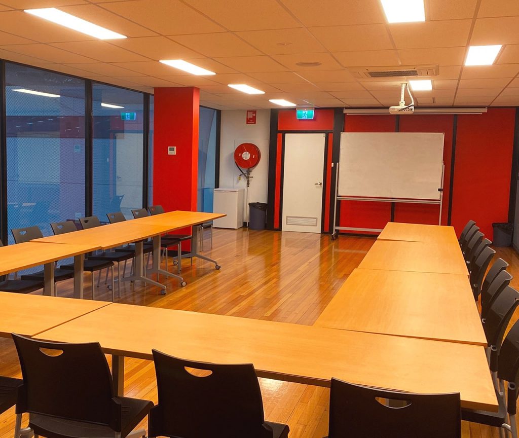 Photo of the meeting room with desks in a u formation facing a whiteboard