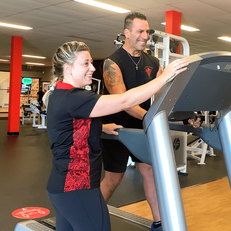 Person working out on a treadmill with PT supervising, both smiling
