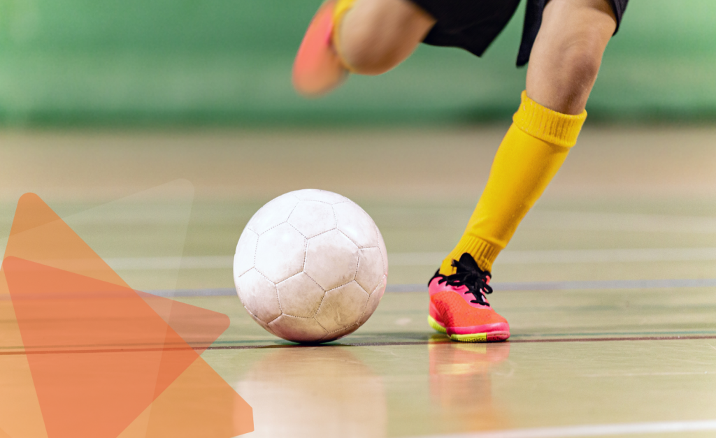 Close-up of a player with yellow socks and pink shoes kicking a futsal ball on an indoor court.