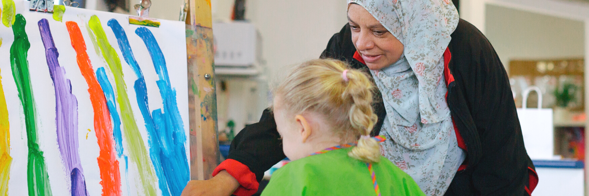 Educator helping a child paint a rainbow